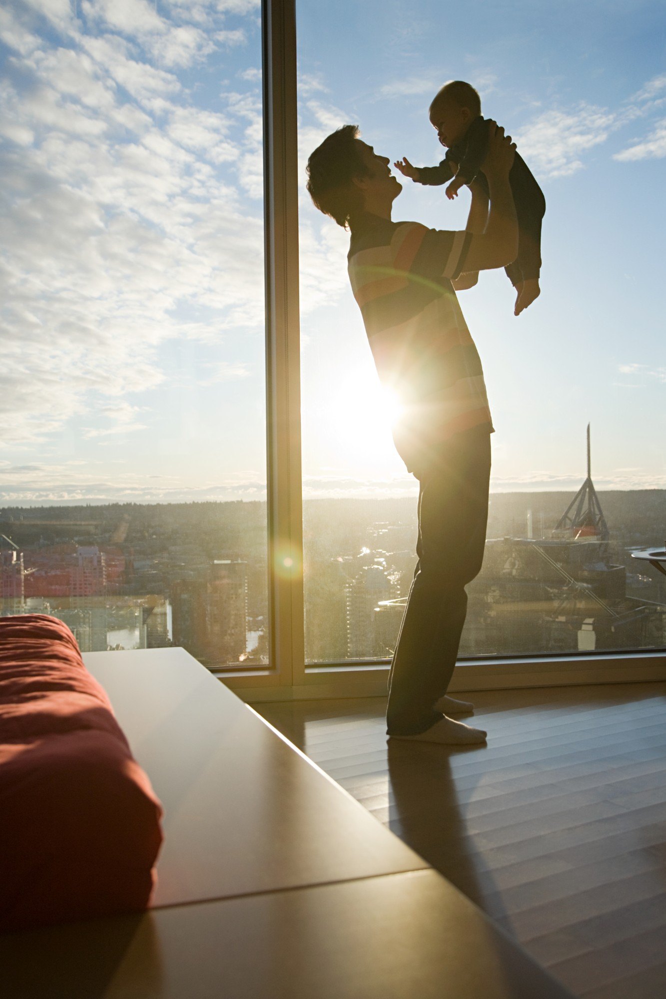 A father lifting his child by a large, sunlit window