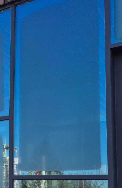 Tau auf der Außenseite eines Dreifach-Isolierglases an einem Wintermorgen; am Rand bleibt das Glas klar